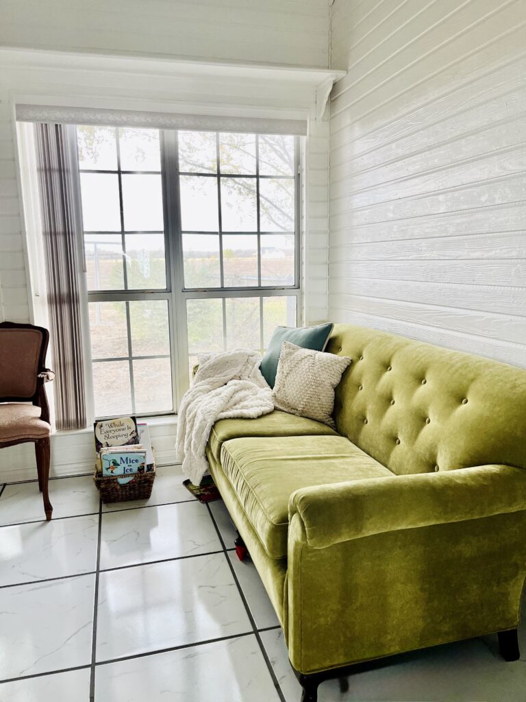 A gorgeous vintage couch in a green color, the sun is breaking forth the very large windows