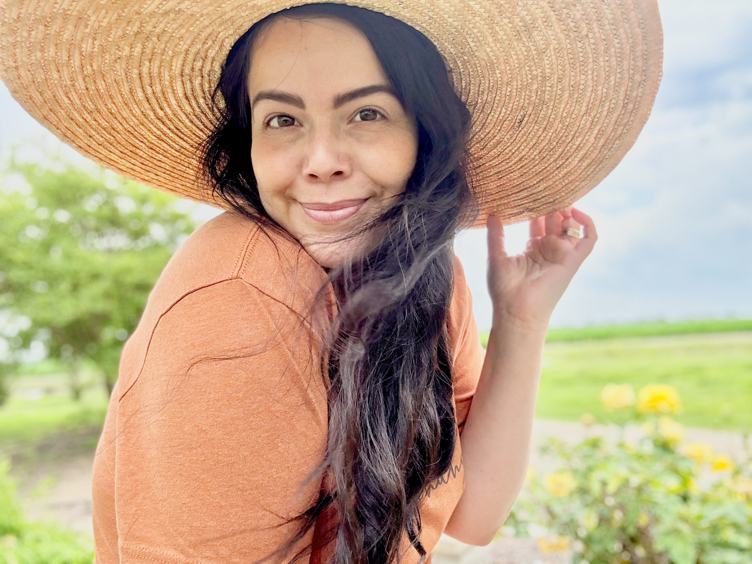 a lovely young woman wearing a large brim hat with one hand on the brim. a gentle smile