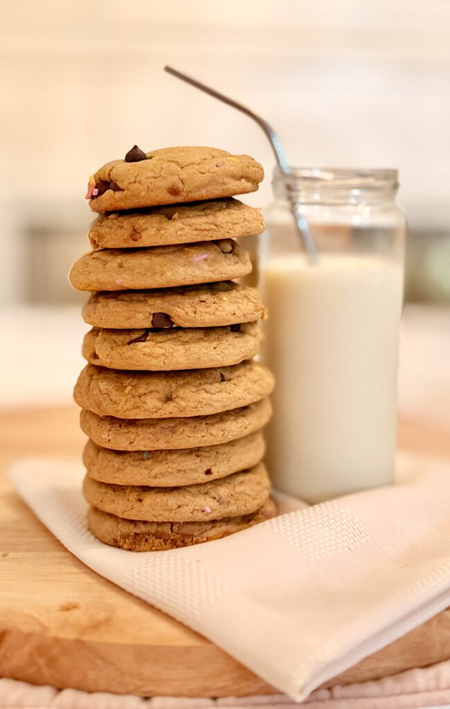 a very tall stack of cookies with a refreshing looking cup of milk and a metal straw peeking through the top of the glass cup