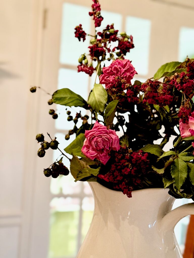 a beautiful up close picture of drying roses with crape myrtle leaves in a large white cottage core pitcher